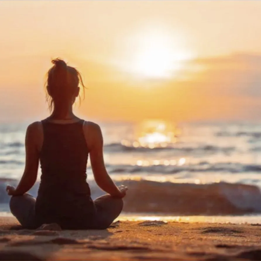 A lady meditating on the beach at sunset