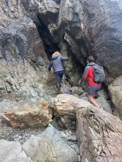 Hikers scrambling over rocks to reach a cave on the Sark coastline