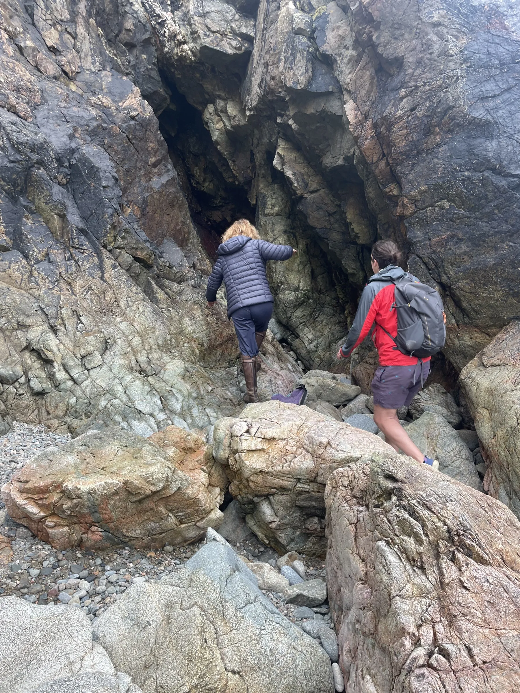 Hikers scrambling over rocks to reach a cave on the Sark coastline
