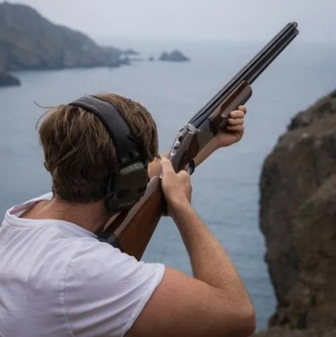 A man aiming a shotgun at a clay pigeon shoot on a Sark clifftop, Sark, Channel Islands