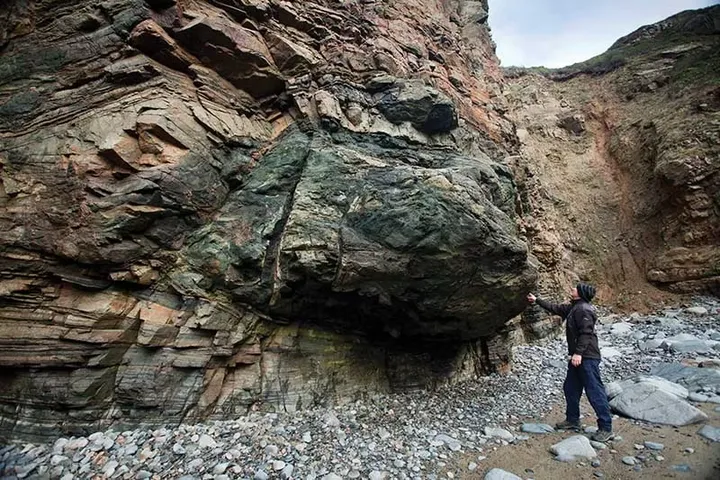Reaching up to a large green rock mass embedded in a layered cliff on Sark, Channel Islands