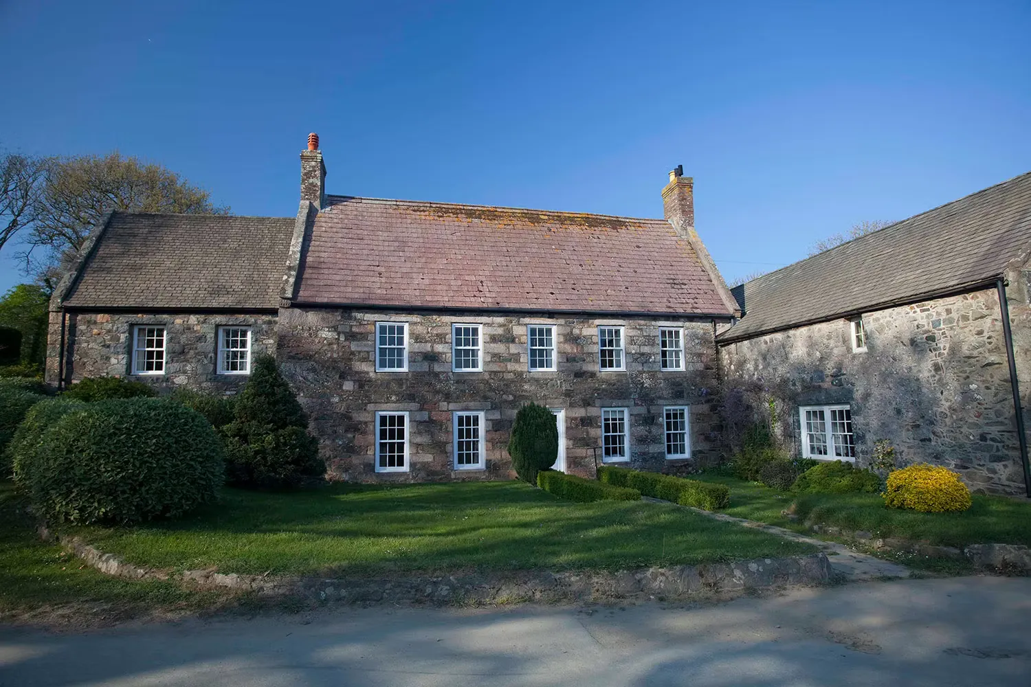 A granite house with white sash windows behind a clipped lawn, Sark, Channel Islands