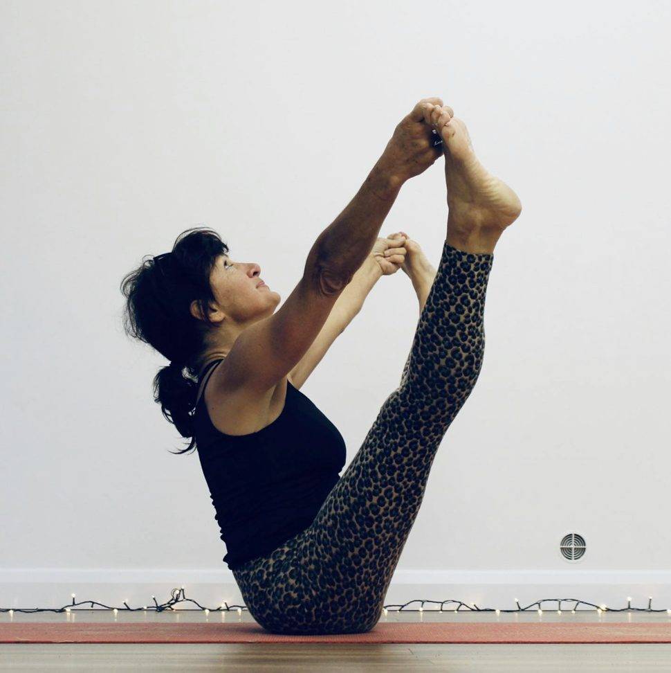 Senior yoga teacher Monica of YogaMorphic practising boat pose in the studio