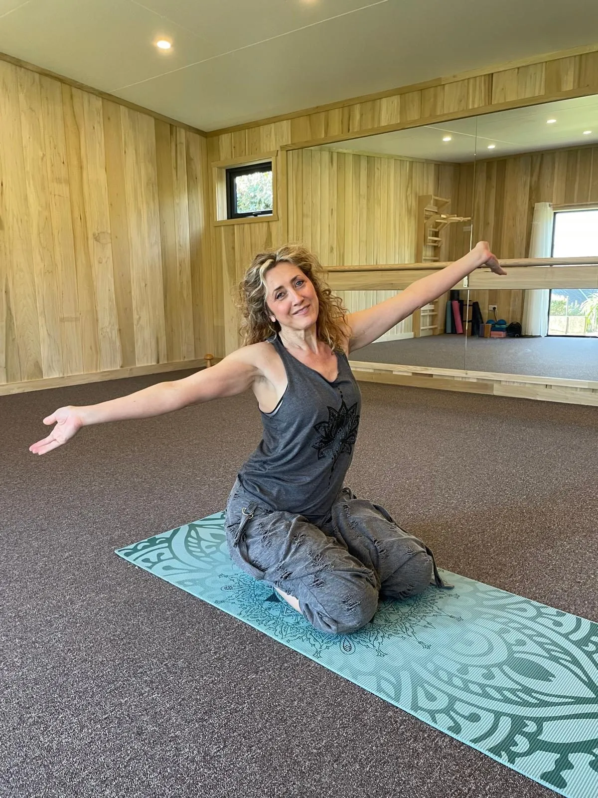 Nadia, founder and host, arms open on the mat in the yoga studio at the retreat house on Sark