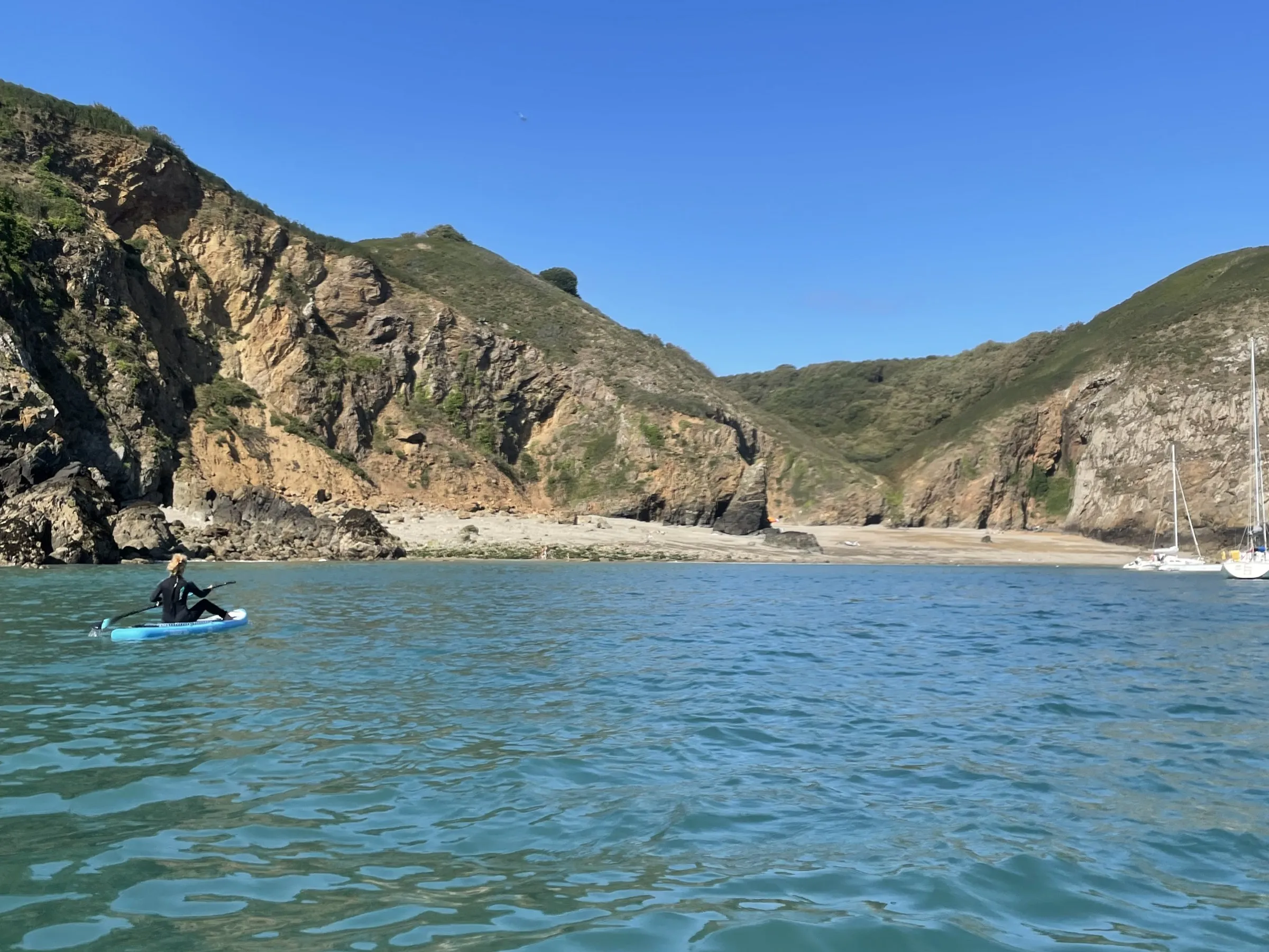 A paddleboarder crossing a clear turquoise bay below the cliffs of Sark