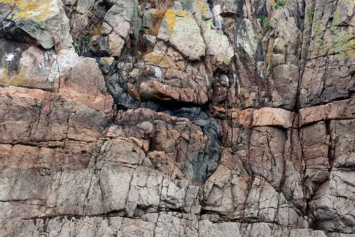A fractured pink and grey cliff face patched with yellow lichen on Sark, Channel Islands