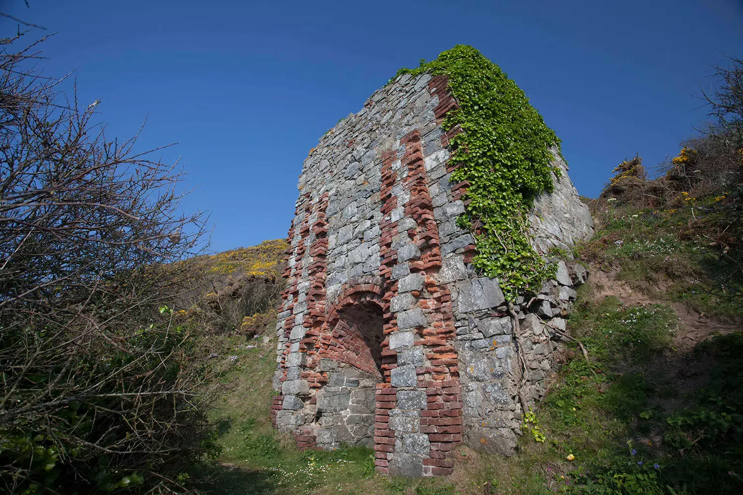 An ivy covered mine ruin with a brick arched opening at Port Gorey on Little Sark, Channel Islands
