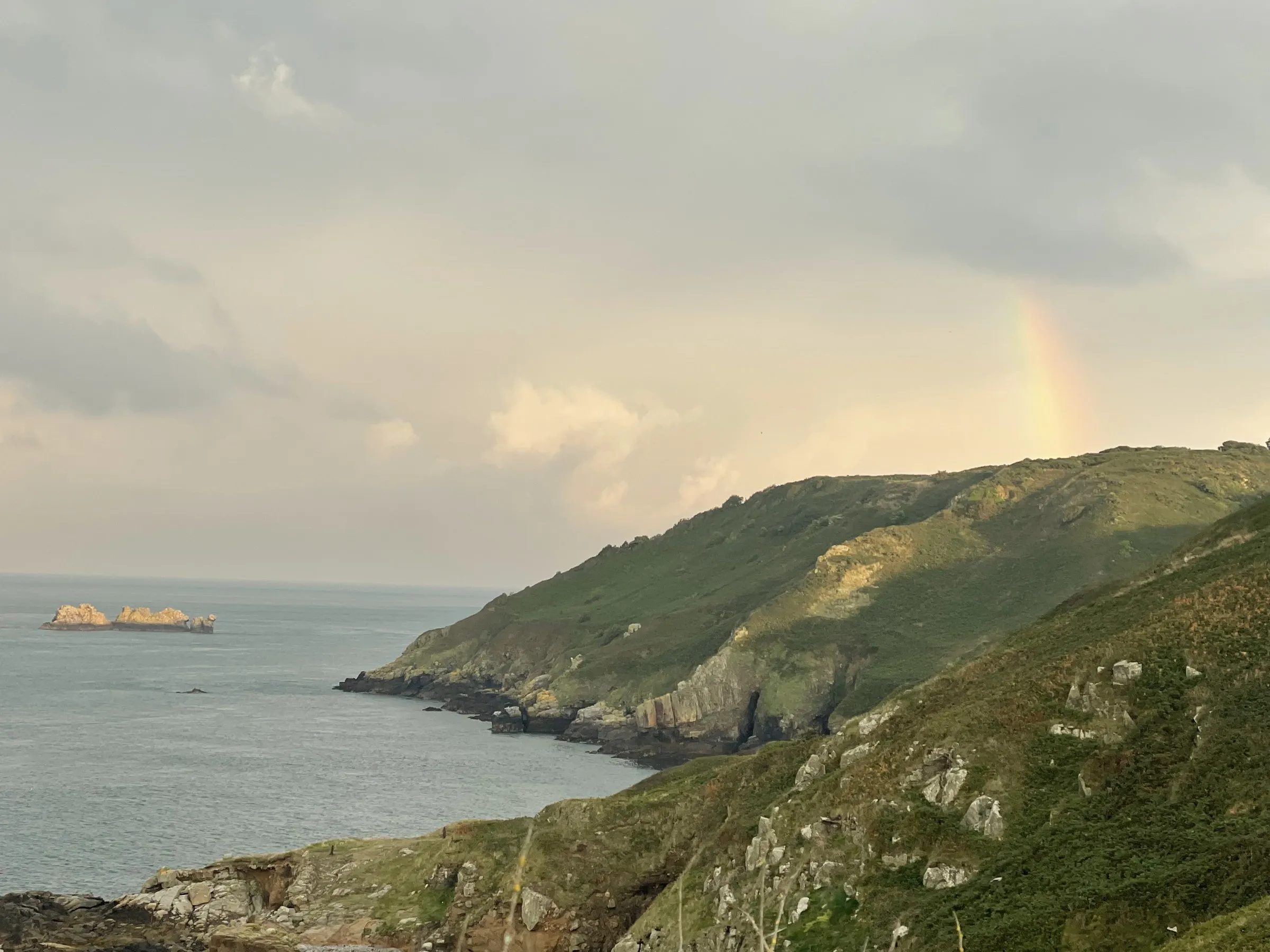 A rainbow rising from the Sark coastline after a rain shower