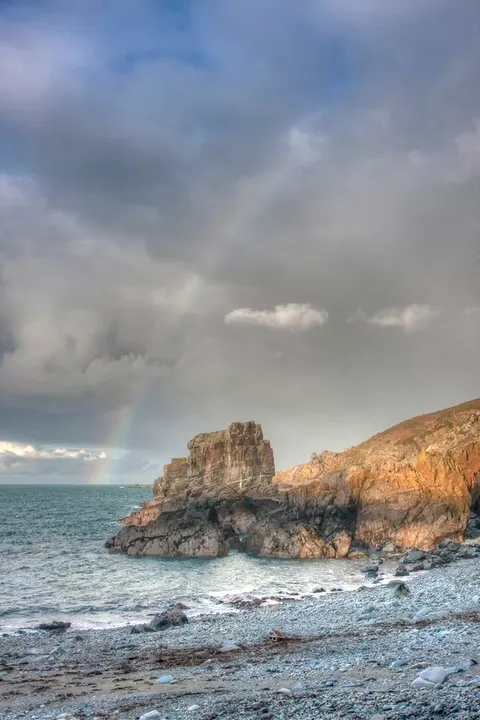 Rain and a rainbow over a rocky headland and shingle beach, Sark, Channel Islands