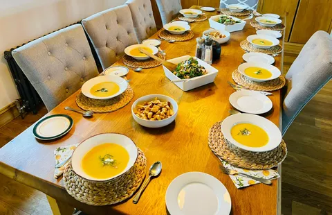 Bowls of soup, a salad and croutons laid out along a long shared dining table