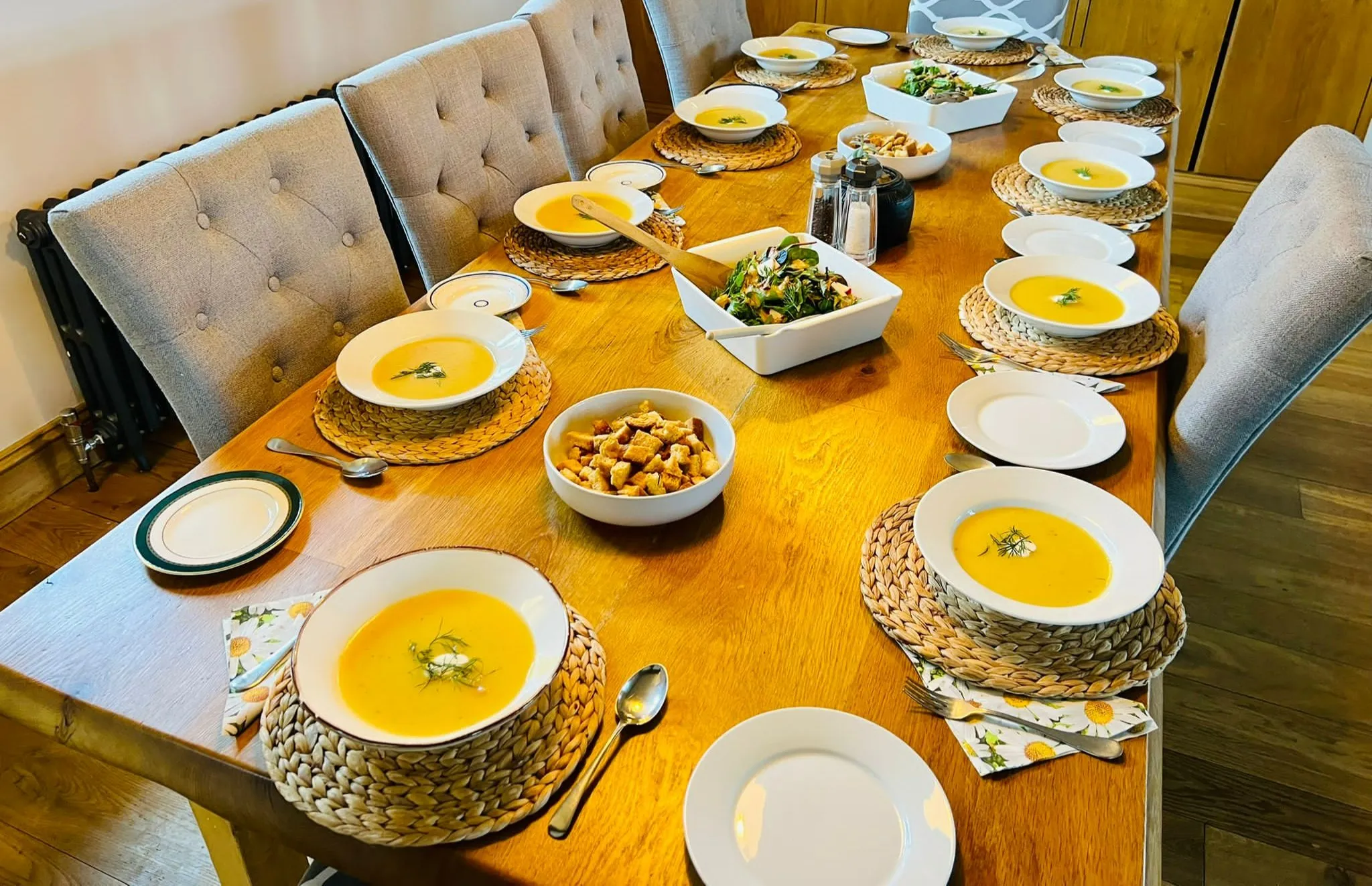 Bowls of soup, a salad and croutons laid out along a long shared dining table