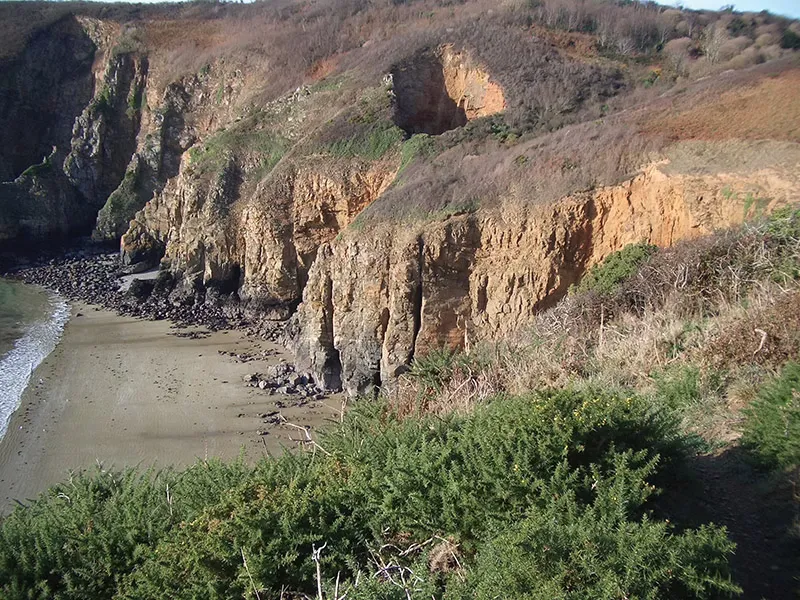 A sandy cove below orange cliffs and gorse, Sark, Channel Islands
