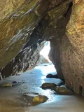 Inside a sea cave on Sark, wet sand and rock lit by daylight through the opening at the far end