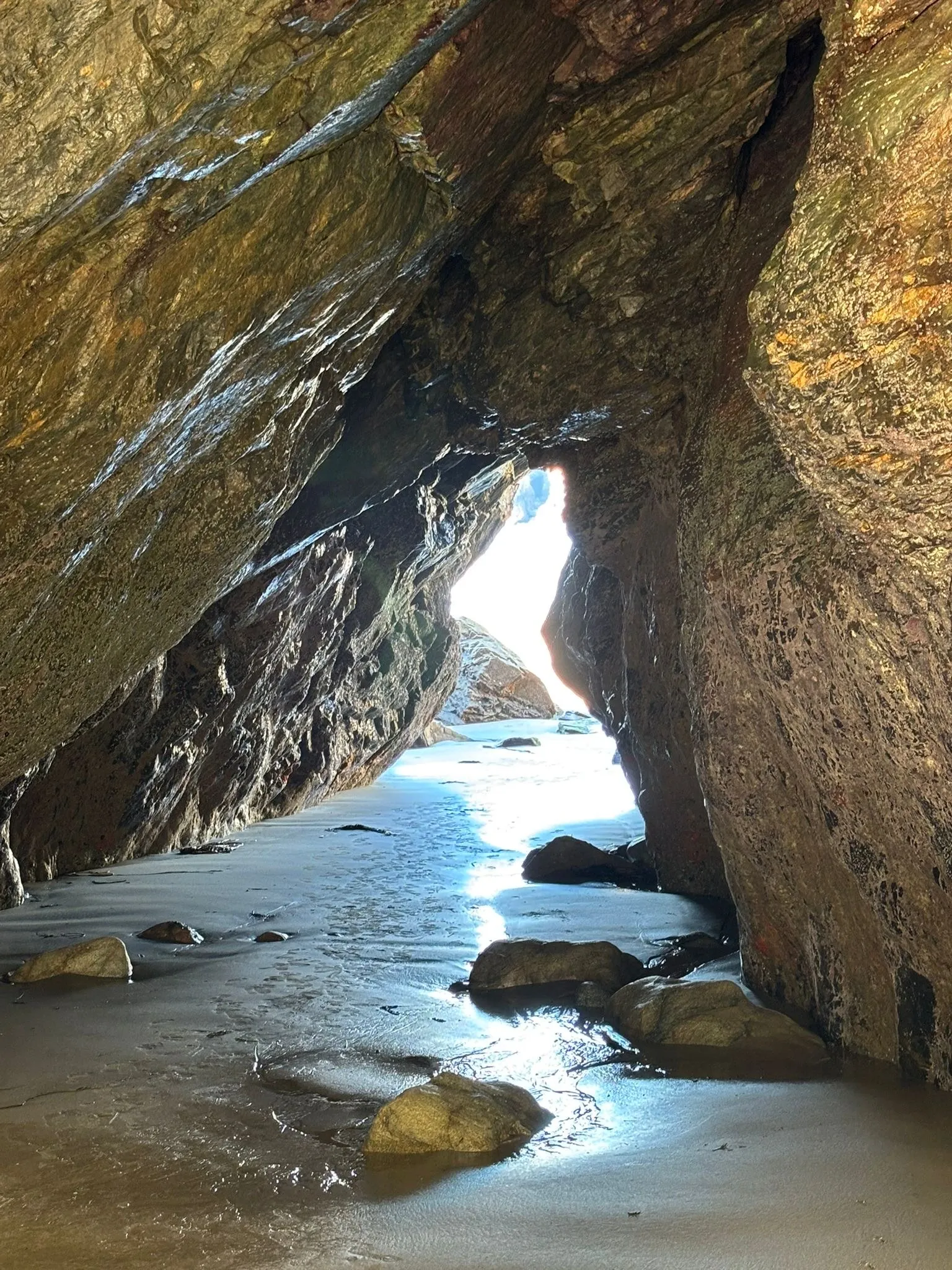 Inside a sea cave on Sark, wet sand and rock lit by daylight through the opening at the far end