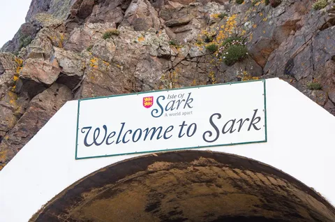 The Welcome to Sark sign above the harbour tunnel, rock face behind, Sark, Channel Islands