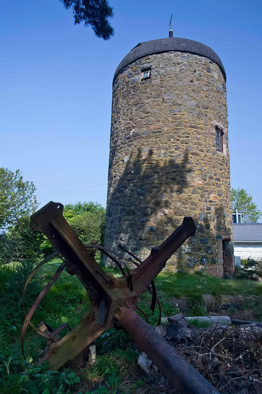 The round stone windmill tower with a rusted horse drawn plough in the foreground, Sark, Channel Islands