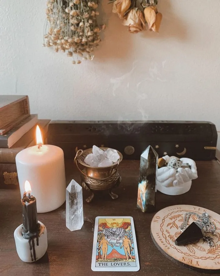 A witchcraft altar with candles, crystals, dried flowers and a tarot card