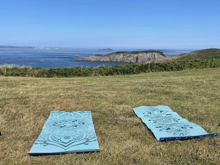 Yoga mats laid out on the clifftop grass above the sea on Sark